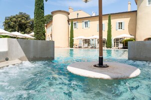 A hot tub surrounded by a pool, with a building in the background.