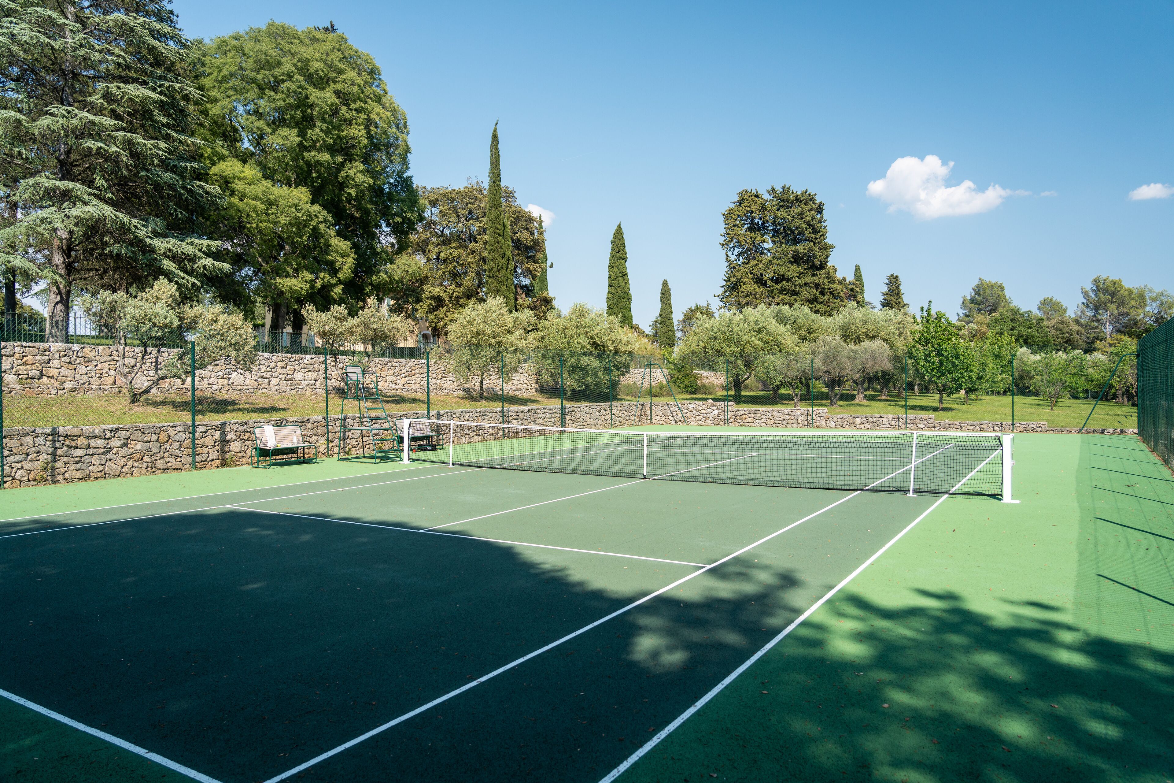Una cancha de tenis con un muro de piedra y árboles al fondo.