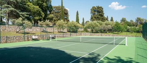 Una cancha de tenis con un muro de piedra y árboles al fondo.