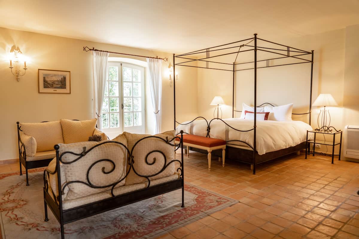 A bedroom with a four-poster bed, a sofa, a small table, and a window with curtains.