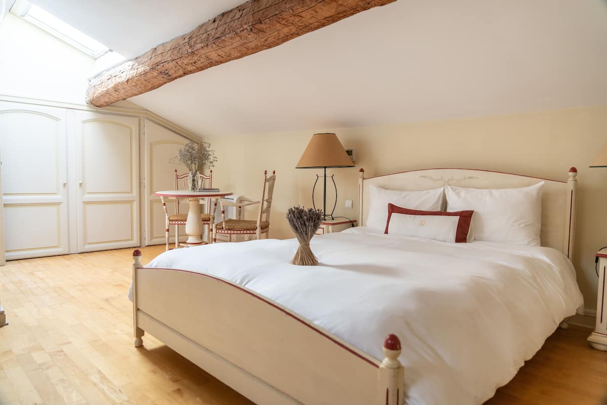 A bedroom with a large bed, a wooden ceiling, a desk with a chair, and a lamp.