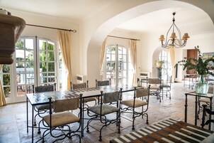 A spacious dining area with a large table and chairs, large windows with curtains, and a chandelier.