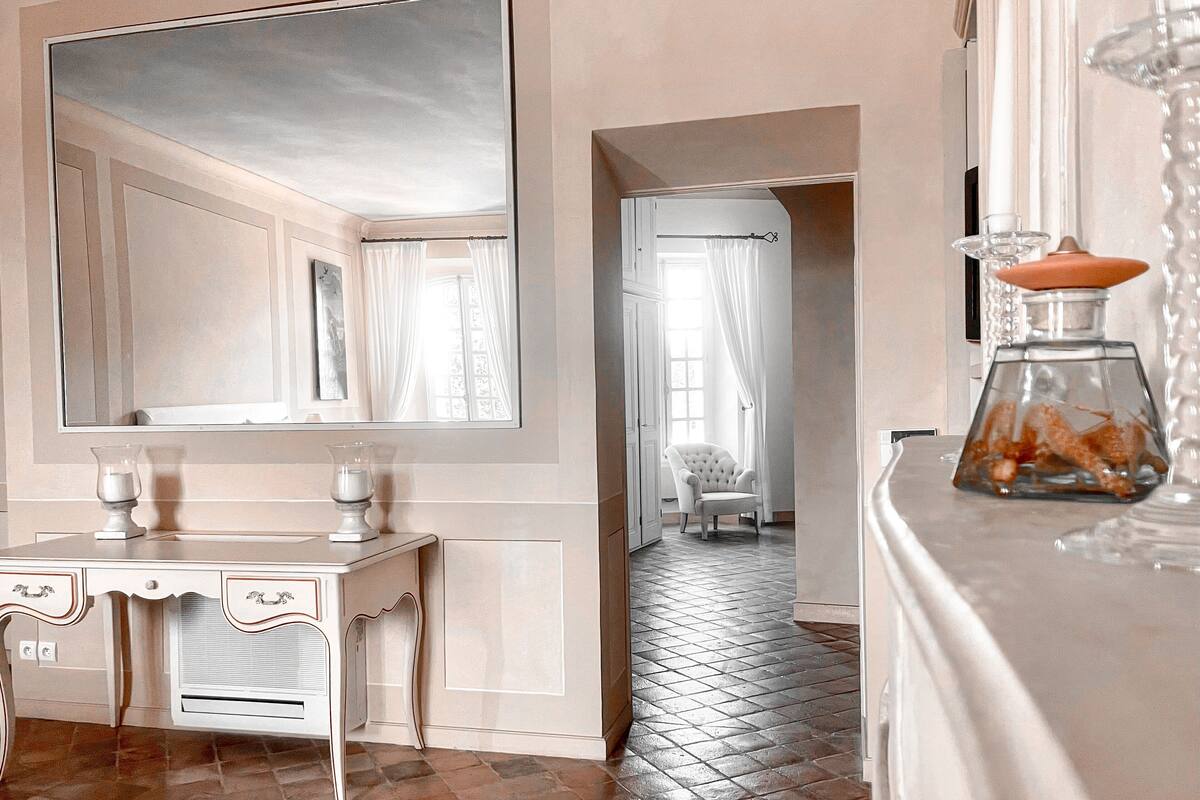 A room with a large mirror, a vanity with a mirror, a chair, and a decorative glass vase.