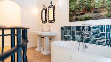 A bathroom with a white bathtub, two sinks, and a large mirror.