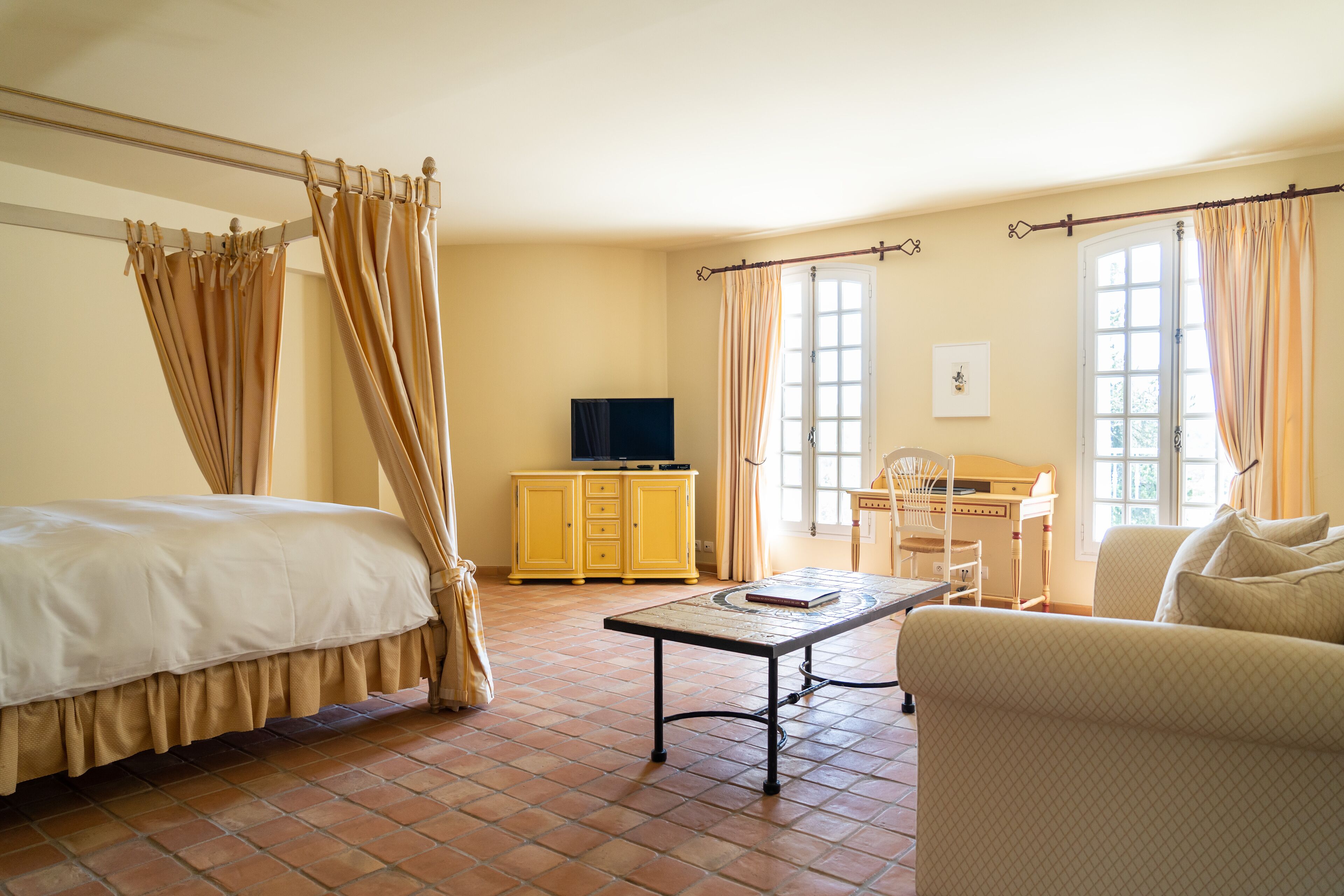 Habitación de hotel con cama, escritorio, silla, televisor y ventana con cortinas.