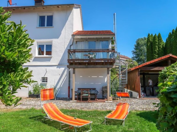A two-story house with a balcony, a covered patio, and two lounge chairs.