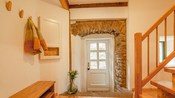 A wooden staircase leading to a stone archway door with a white panel. - Rustic Eifel - Garden, kitchen - Hiking, bike trails & self-check-in (Gerolstein)