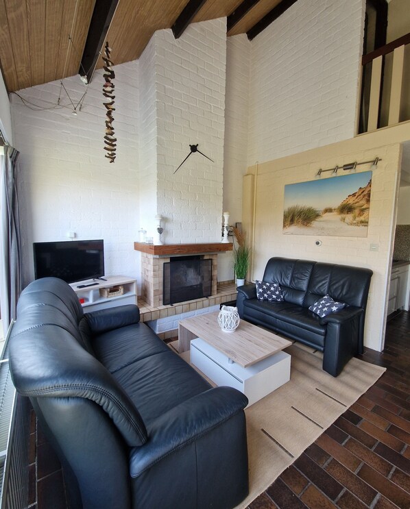 A living room with a black leather sofa, a white coffee table, a fireplace, and a painting on the wall. - Vacation home by the sea, Holland, family-friendly park, De Kreek, WLAN free!!! (Bruinisse)