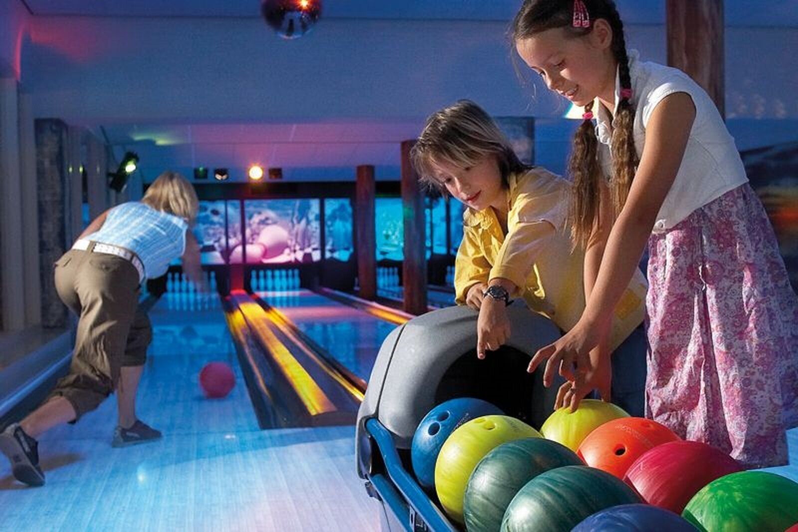 Een bowlingbaan met banen, bowlingballen en een persoon die aan het bowlen is.