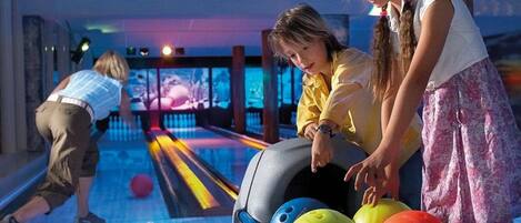 Een bowlingbaan met banen, bowlingballen en een persoon die aan het bowlen is.