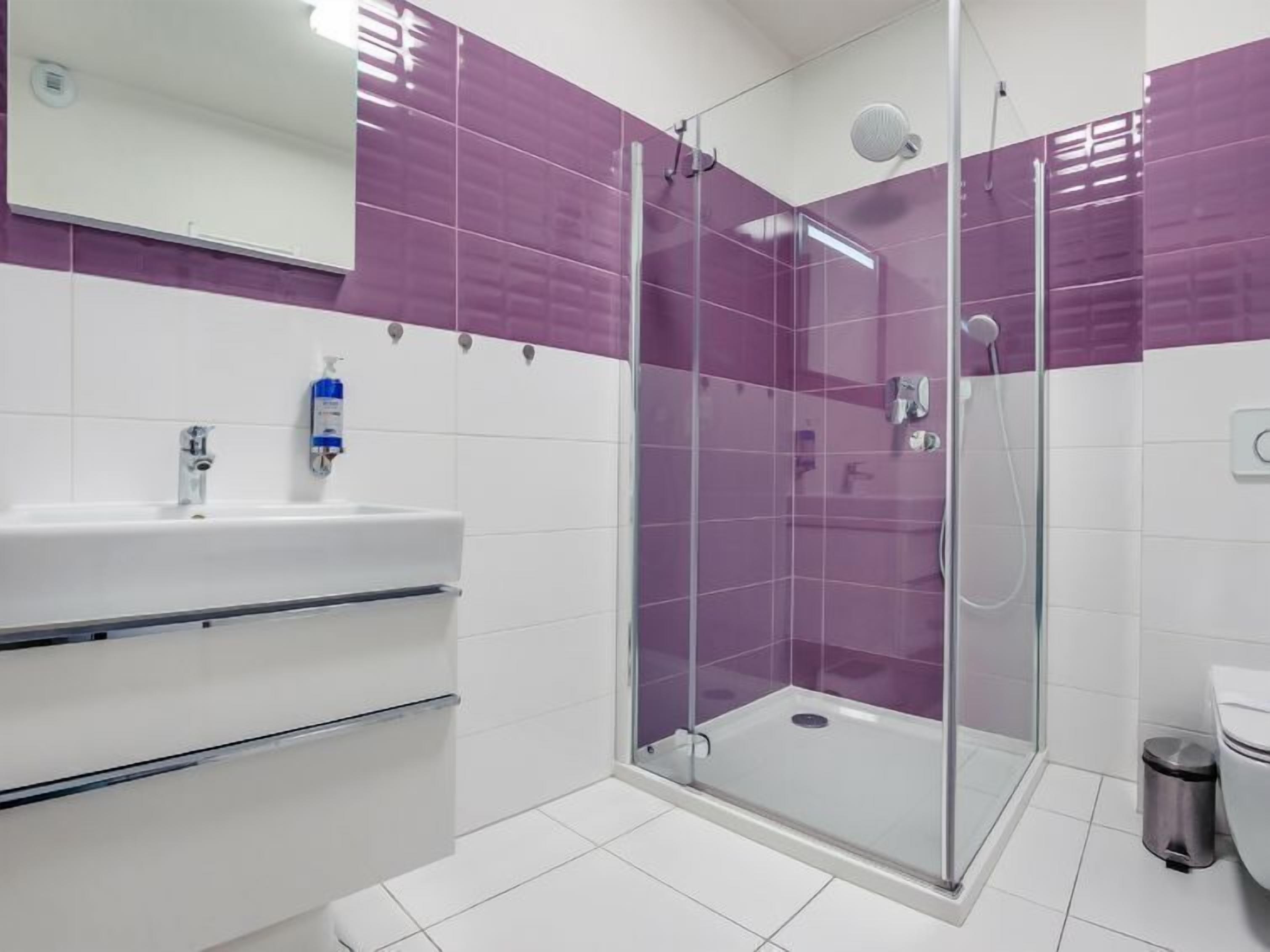 A modern bathroom with a glass-enclosed shower, white sink, and purple-tiled walls.