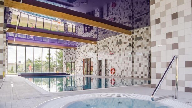 Ein moderner Innenpool mit Whirlpool, großen Fenstern und einem Schachbrettmuster an der Wand.