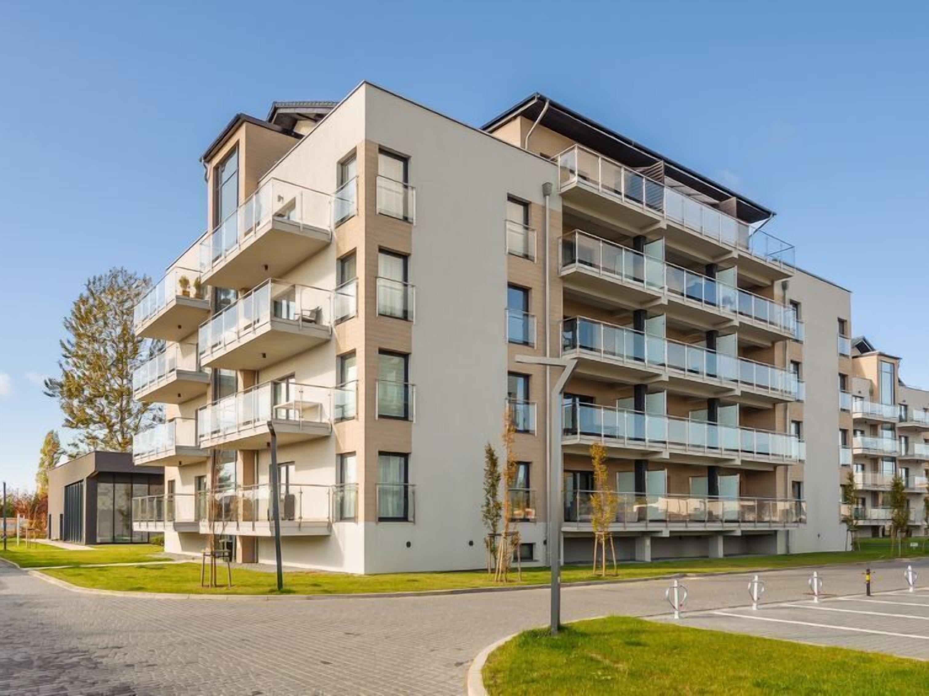 En flervåningsbostadsbyggnad med balkonger, en asfalterad uppfart och en gräsyta.
