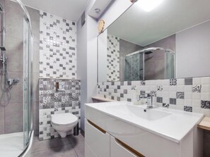 Contemporary bathroom with a glass-enclosed shower, white toilet, and large mirror above a sink with a wooden countertop.