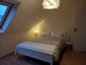 A bedroom with a sloped ceiling, a bed with patterned bedding, a bedside lamp, and a small table with a chair.