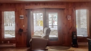 Un interior de madera con un sillón blanco, una puerta que da al exterior y un estante con objetos.