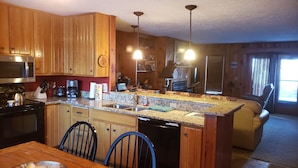 Cocina con gabinetes de madera, encimera de granito, pileta, microondas, estufa y lavavajillas. Hay un comedor con mesa y sillas.