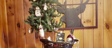 Un interior de madera con una mesa redonda, dos sillas estampadas, un árbol de Navidad y un adorno en la pared.