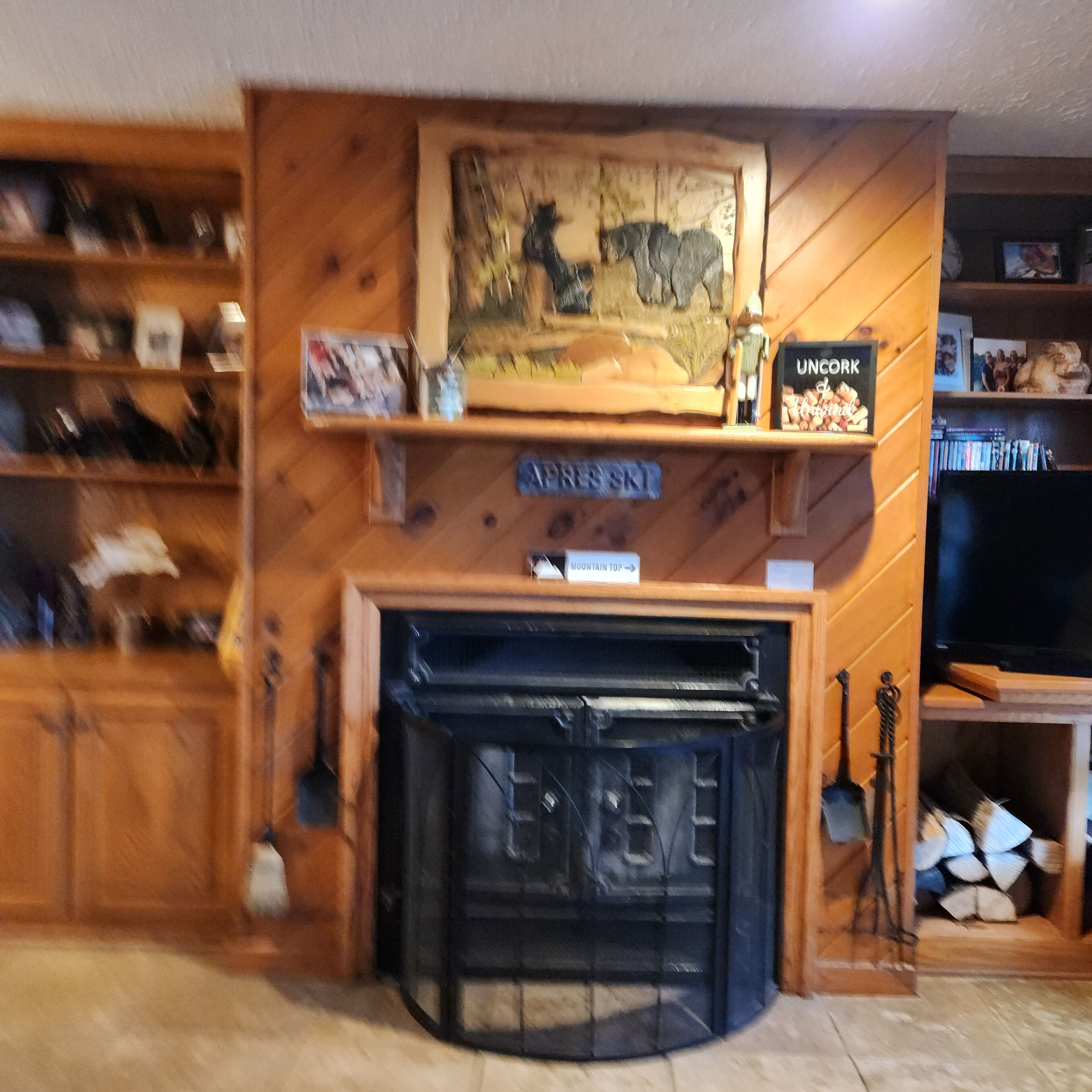 A wooden interior with a fireplace, shelves with books and decorative items, and a sign reading "MOUNTAIN TOP".