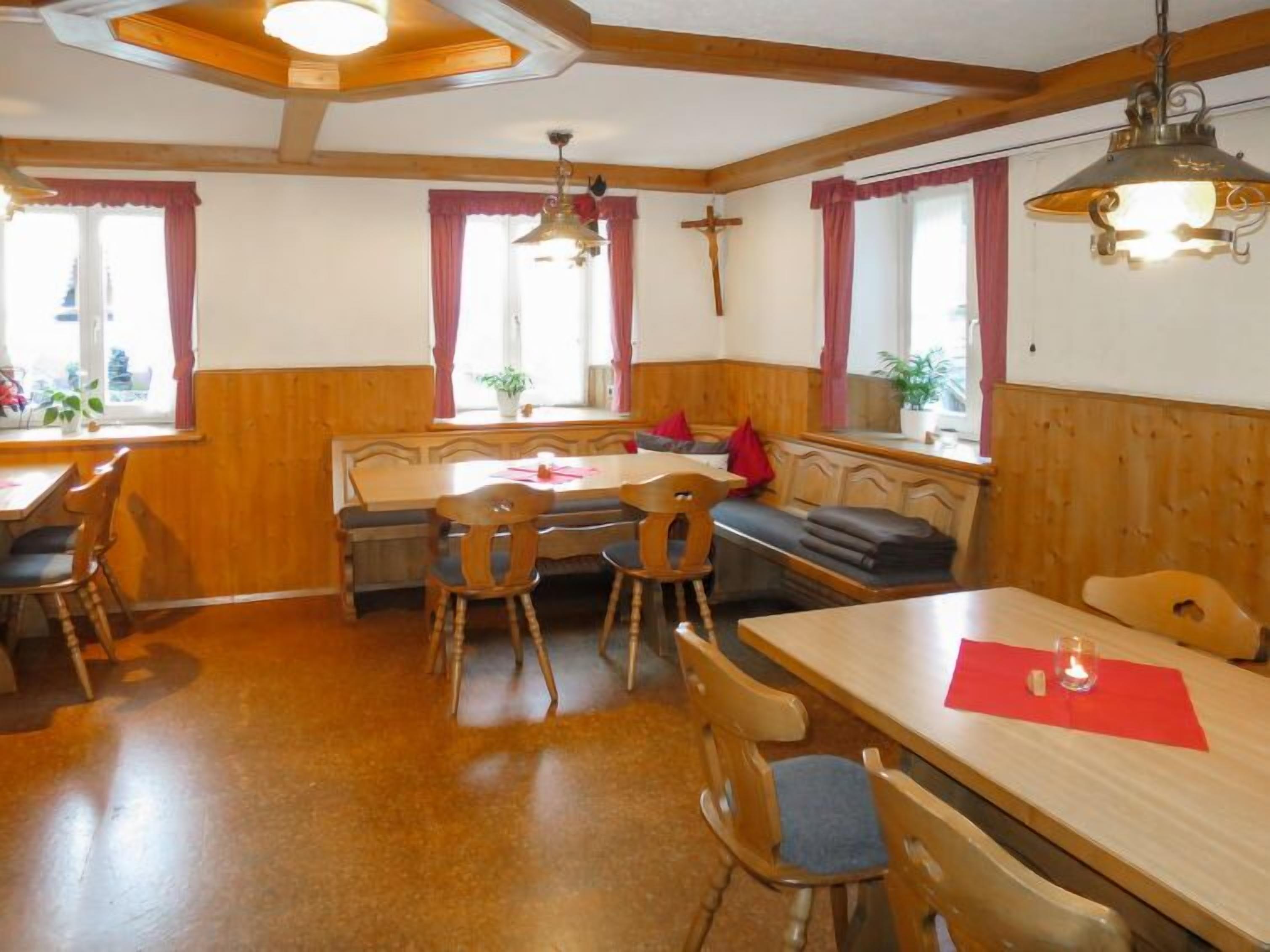 A cozy dining area with wooden furniture, a cross on the wall, and a window with curtains.