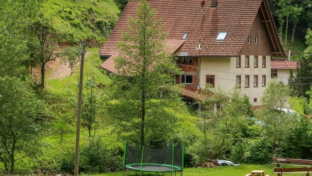 Ein Haus mit geneigtem Dach, umgeben von üppigem Grün und einem Trampolin im Garten.