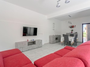 Un salon moderne doté d’un téléviseur à écran plat, d’un meuble de rangement gris et de sièges recouverts d’un tissu rouge.