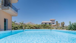 Una piscina azul cristalina rodeada de vegetación y un edificio con balcón.