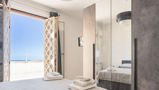 Un dormitorio moderno con una cama grande, cabina de ducha de vidrio y vista a la playa.