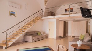 Amplia sala de estar con escalera, sofá, mesa de centro y televisor montado en la pared.