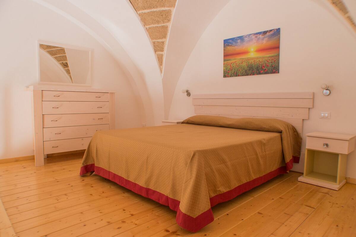 Un dormitorio con una cama, un tocador, una mesita de noche y un cuadro de un atardecer.