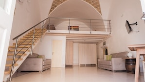 Amplia sala de estar con techo alto, escalera de madera y balcón.