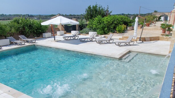 Una piscina con agua cristalina, rodeada de sillones de baño y sombrillas.