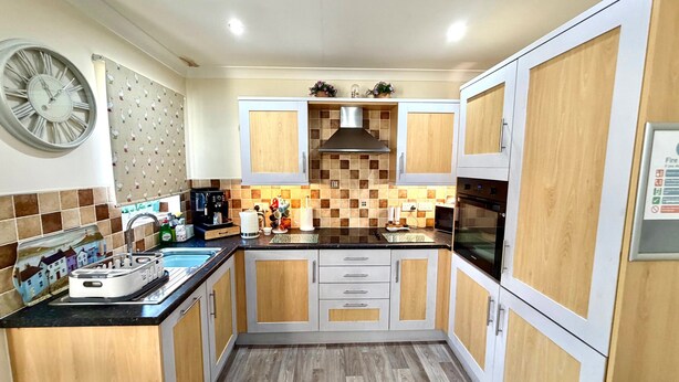A compact kitchen with wooden cabinets, a black countertop, a stainless steel sink, and a clock on the wall. - Apartment 1 (Morecambe)