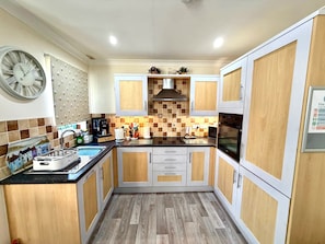 A compact kitchen with wooden cabinets, a black countertop, a stainless steel sink, and a clock on the wall. - Apartment 1 (Morecambe)