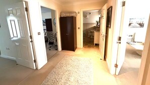 A hallway with a carpet, a door with a sign, a chair, and a view into a bathroom. - Apartment 1 (Morecambe)