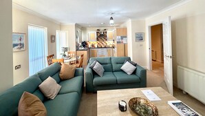 A modern living room with two green sofas, a coffee table, and a kitchen in the background. - Apartment 1 (Morecambe)