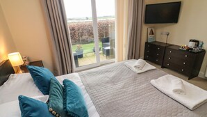 A hotel room with a large bed, a flat-screen TV, a dresser, and a view of a garden through a sliding glass door. - Apartment 1 (Morecambe)