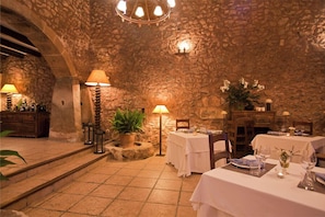 A stone-walled interior with tables set for dining, ambient lighting, and potted plants.