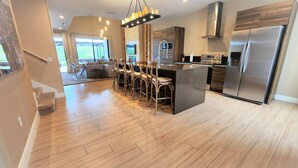 Une cuisine moderne dotée d’un îlot central, d’appareils électroménagers en acier inoxydable et d’un coin repas avec des chaises en bois.