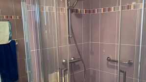 Una ducha con cerramiento de vidrio, con cabezal de ducha manual y un accesorio de ducha manual.