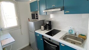 Una cocina compacta con armarios color turquesa, una encimera blanca, un lavamanos de acero inoxidable, un microondas, una cafetera y un pequeño cubo de basura.