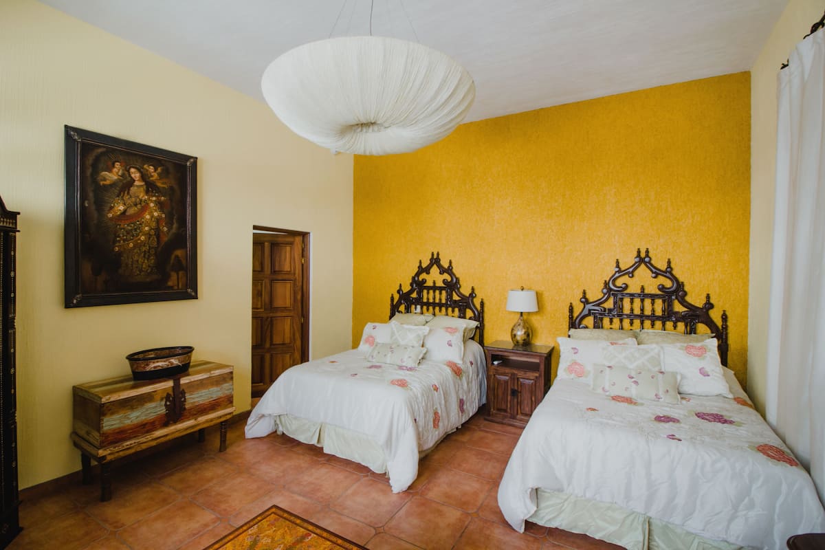 Ein Schlafzimmer mit zwei Betten, einem Holzkopfende, einem Nachttisch mit Lampe, einer Bank und einem Bild an der Wand.