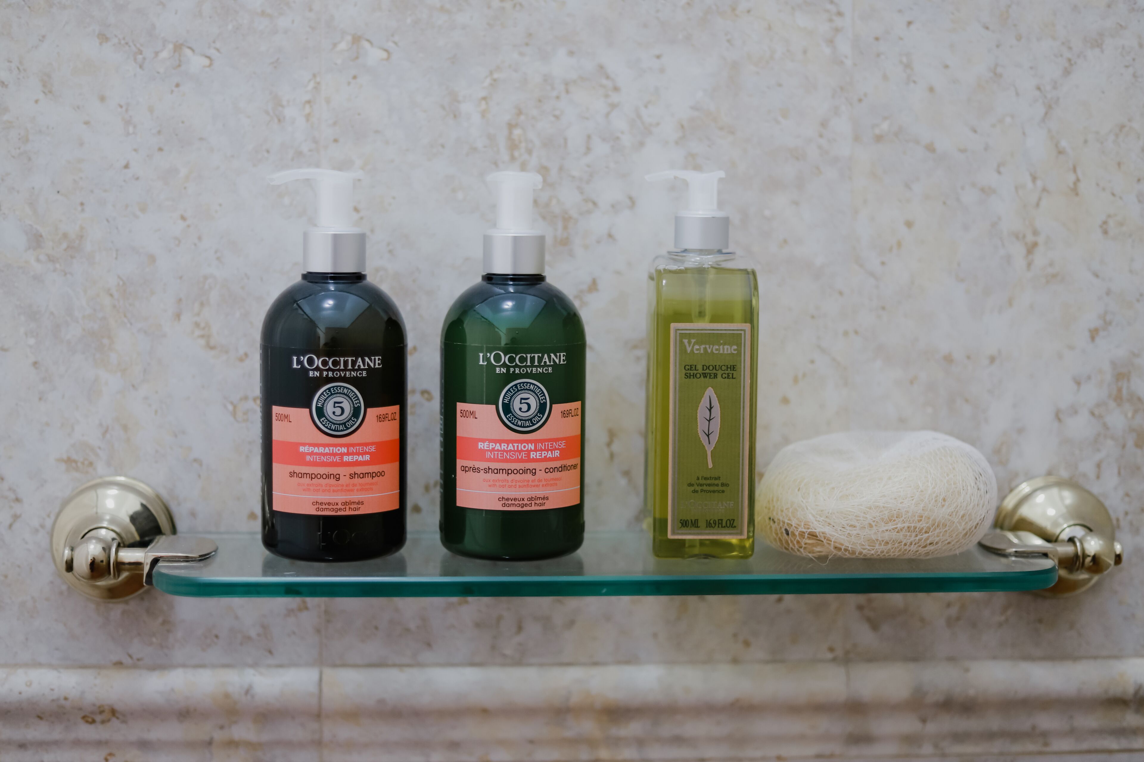 Estante de baño con tres botellas de champú y acondicionador de L'OCCITANE, y un gel de ducha Verveine.
