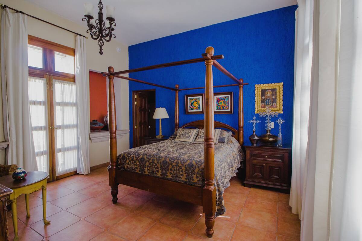 Ein Raum mit blauen Wänden, einem Holznachttisch und einem Tisch mit einer Lampe, in dem ein Bett mit Baldachin steht.