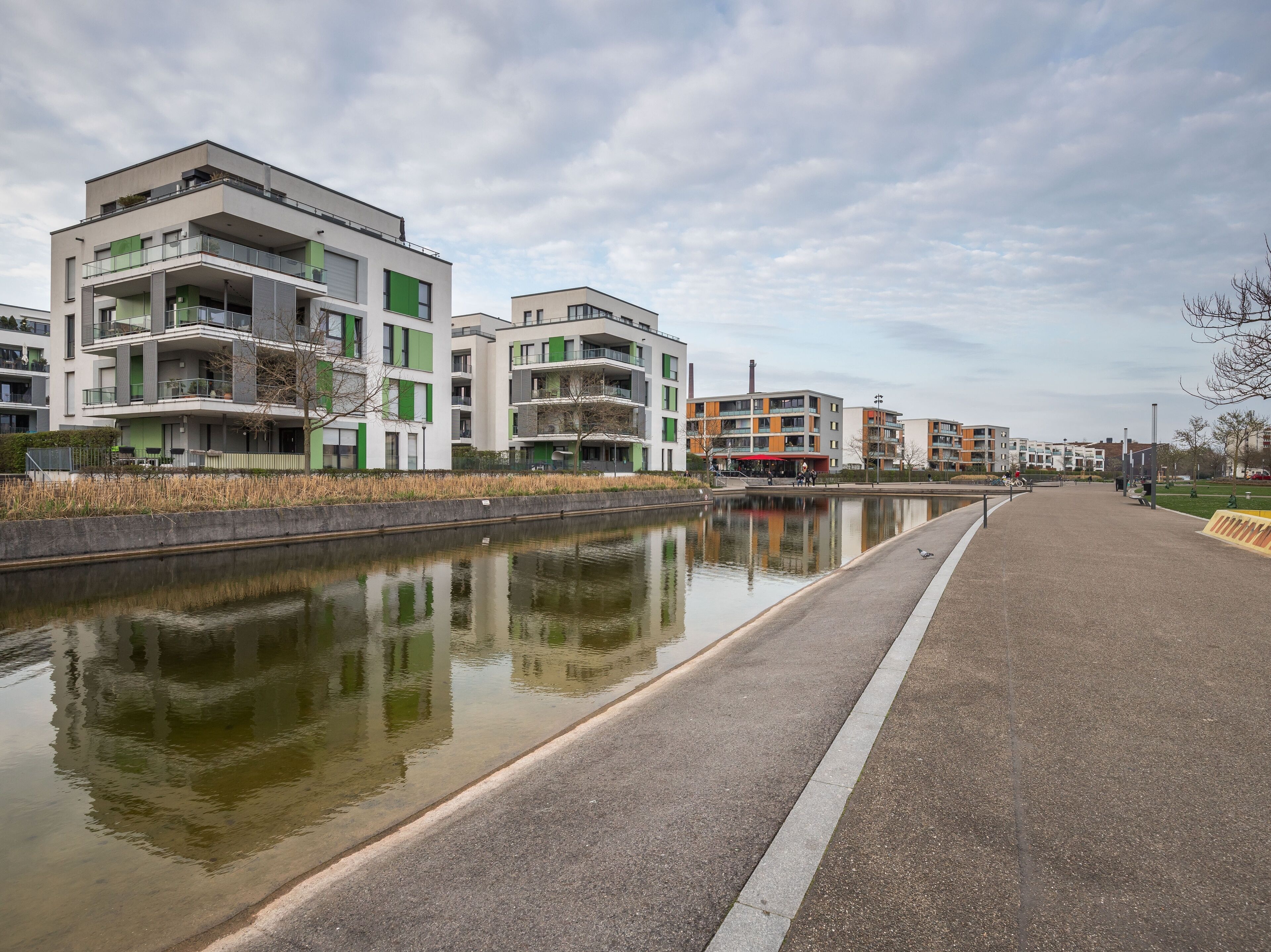 A modern residential area with multi-story buildings, a canal, and a paved walkway.