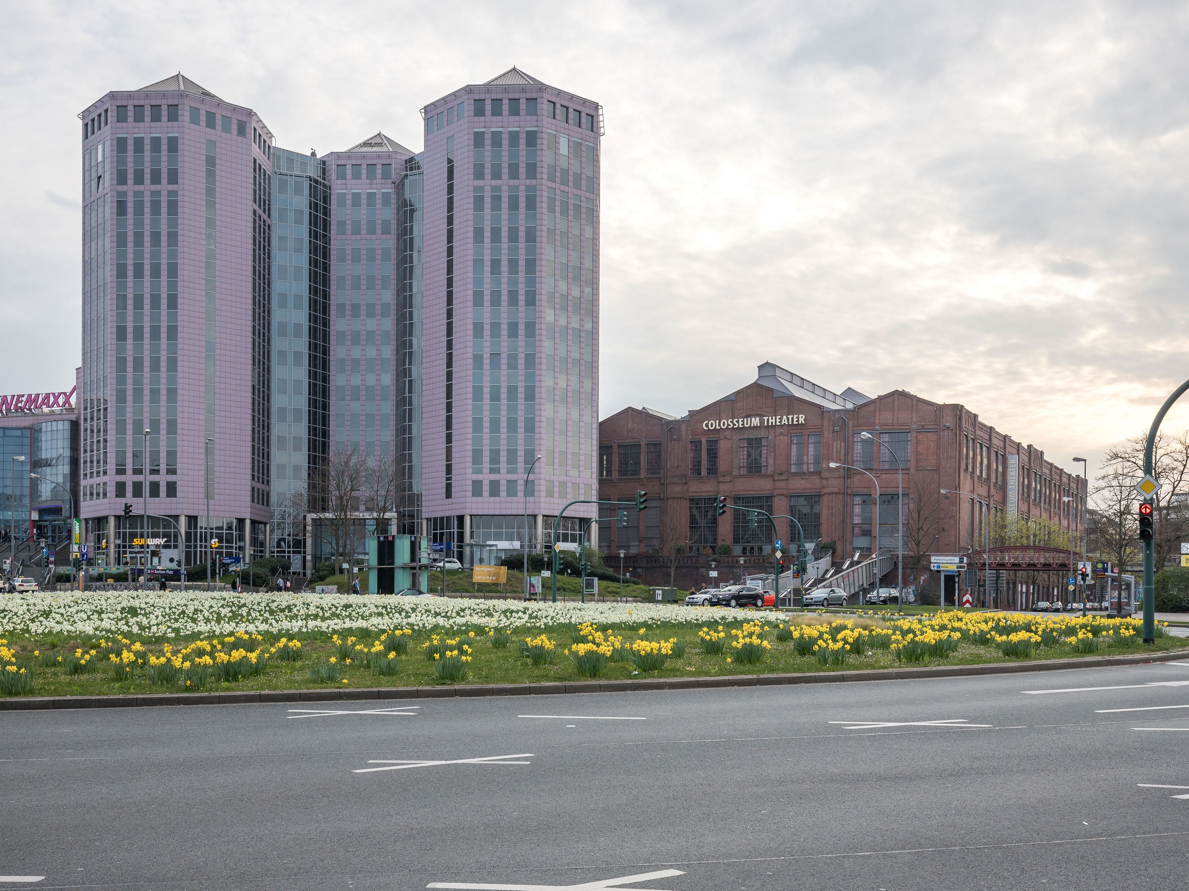 A modern building with a glass facade and a brick structure labeled "Colosseum Theater" in the background.