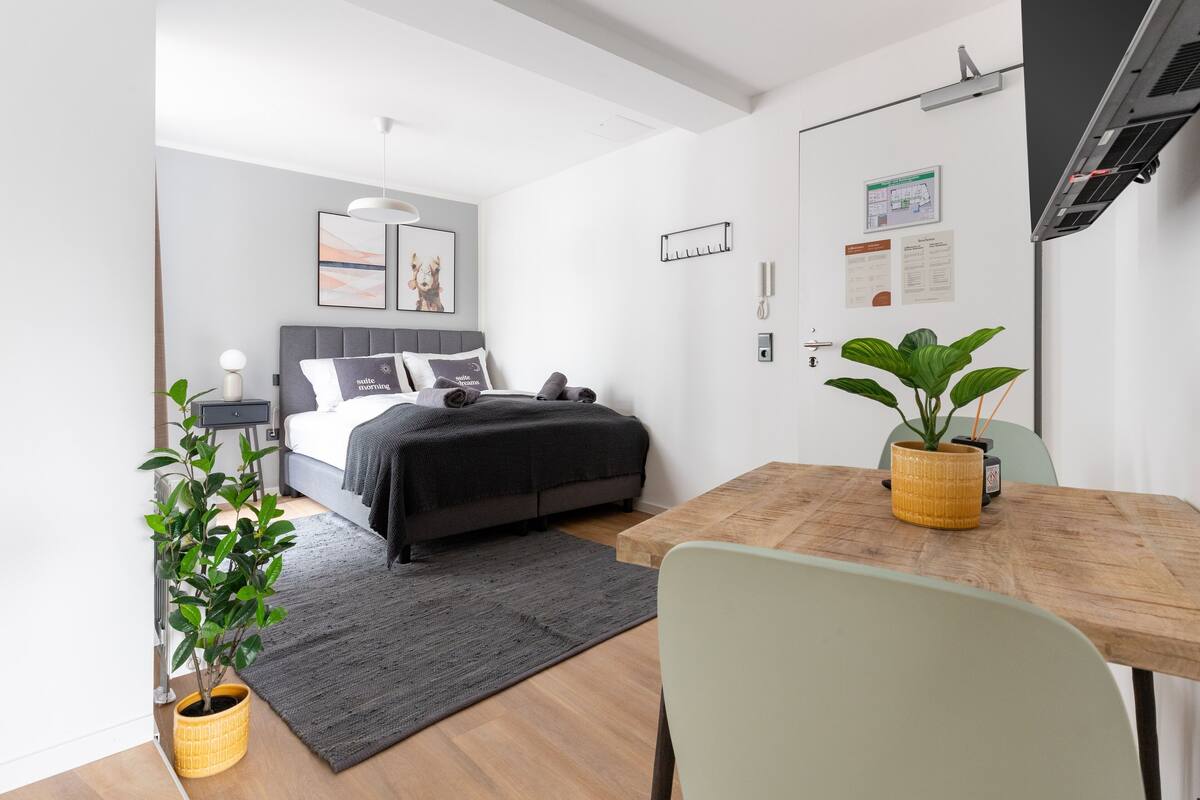Un dormitorio moderno con cama, mesita de noche, lámpara y una planta en maceta.