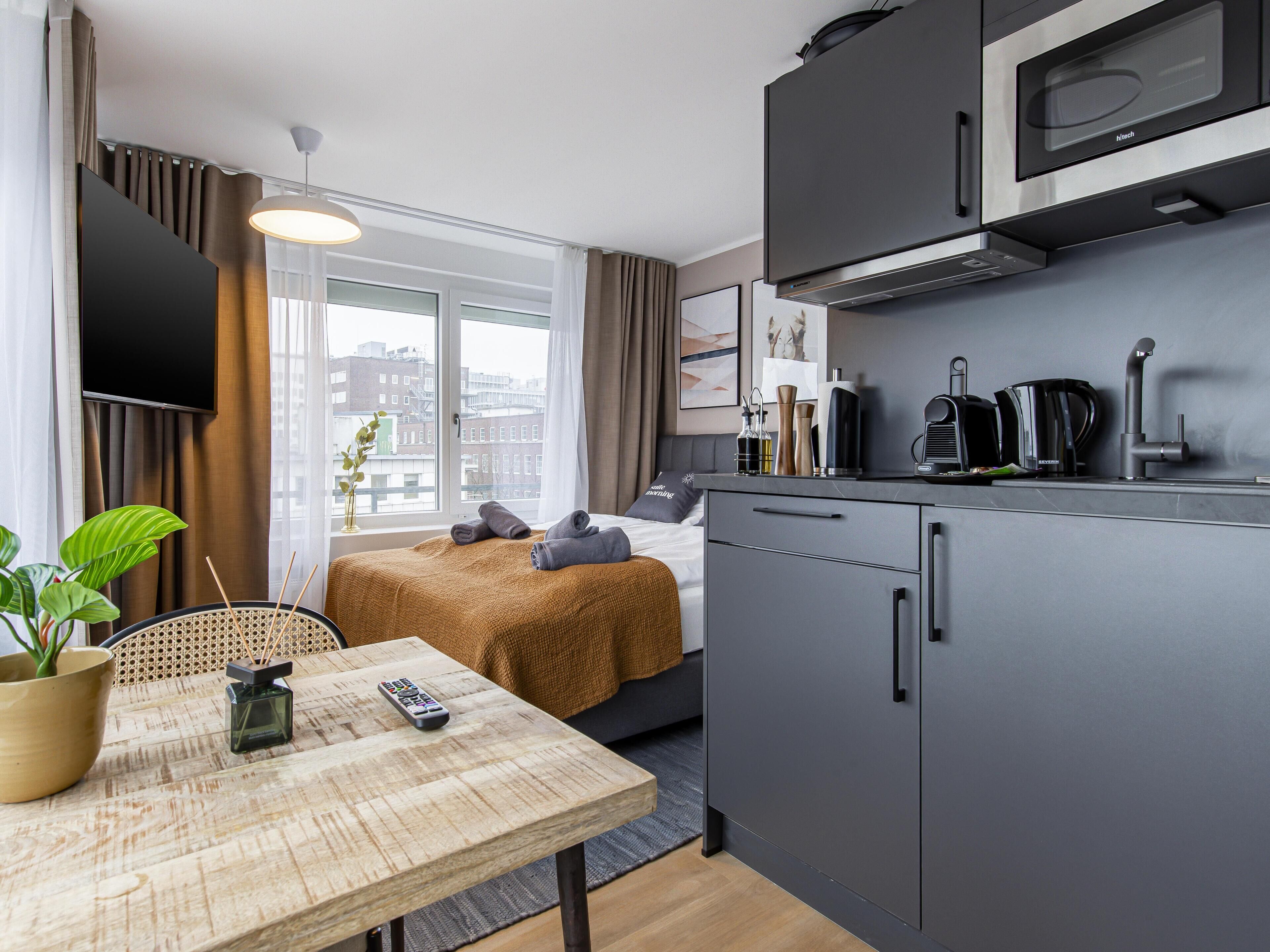 Una camera d'albergo moderna con un letto, un tavolo da pranzo, angolo cottura e vista sulla città.