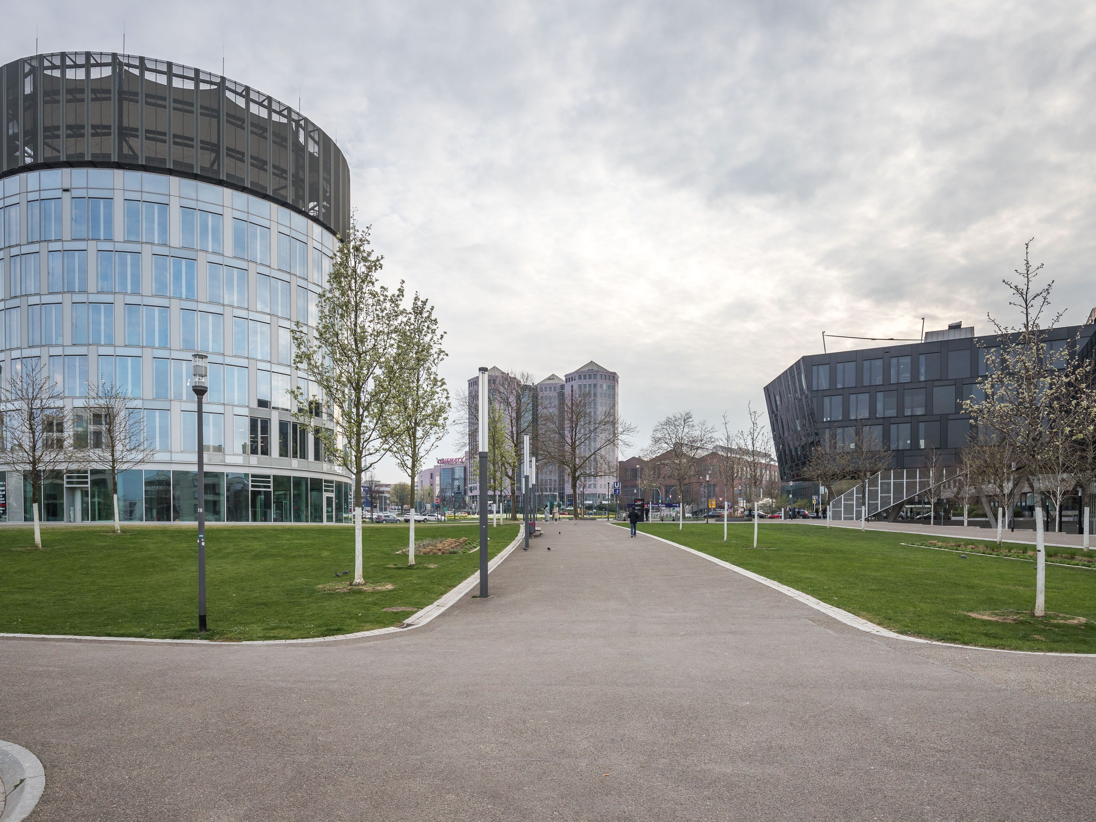 A modern urban plaza with a curved building, green lawns, and a clear sky.