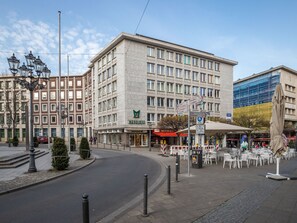 A multi-story hotel with a prominent 'MEPHISTO' sign, outdoor seating area, and a modern building with glass facade in the background. - Limehome Essen Kettwiger Str. (Essen)